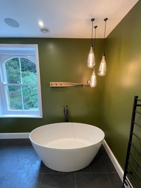 Modern bathroom with a freestanding white tub and green walls under warm pendant lights.
