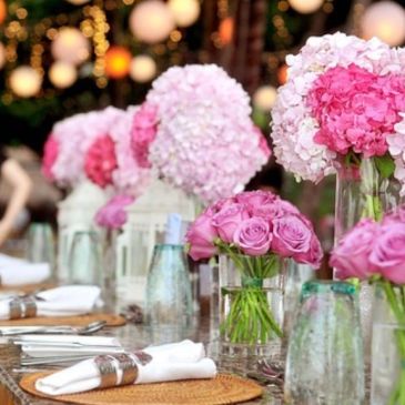 Elegant table setting with pink and white floral centerpieces and neatly folded napkins.