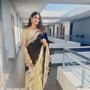 Woman in elegant black and gold saree standing in a modern corridor.