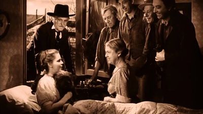A group of people gather around a woman lying in bed, sharing a moment.