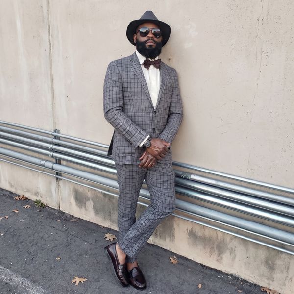 Man in a stylish checked suit, hat, and sunglasses leaning against a wall. Concrete King LLC, Brian Gaines Sr.