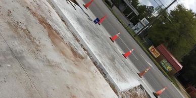 Freshly poured concrete section marked with traffic cones along a roadside.