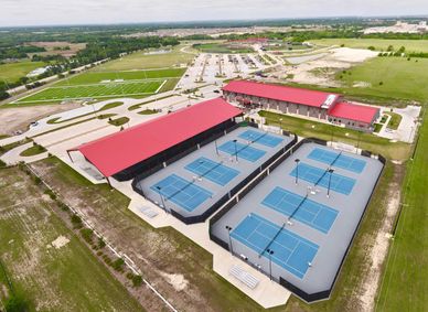 Aerial view of a sports complex with multiple tennis courts and red-roofed buildings.