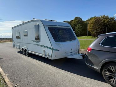 A car towing a white caravan on a sunny day.