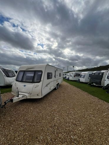A caravan parked on a gravel path under a cloudy sky.