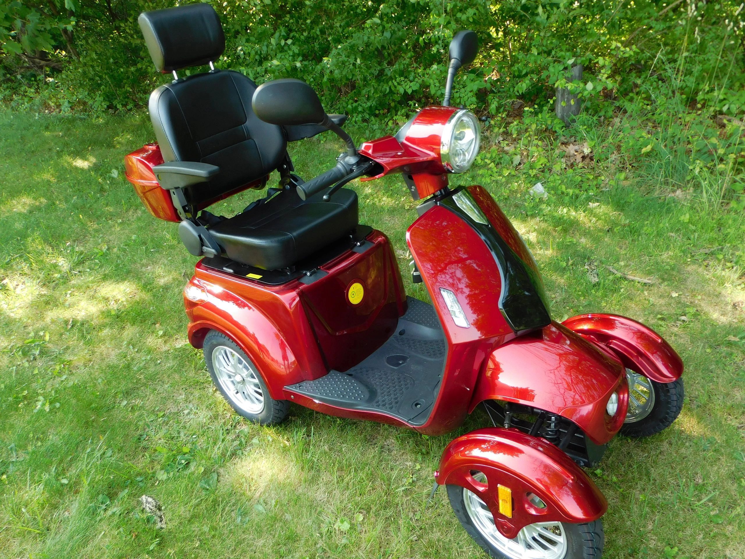 A shiny red mobility scooter with a black seat on grass.
