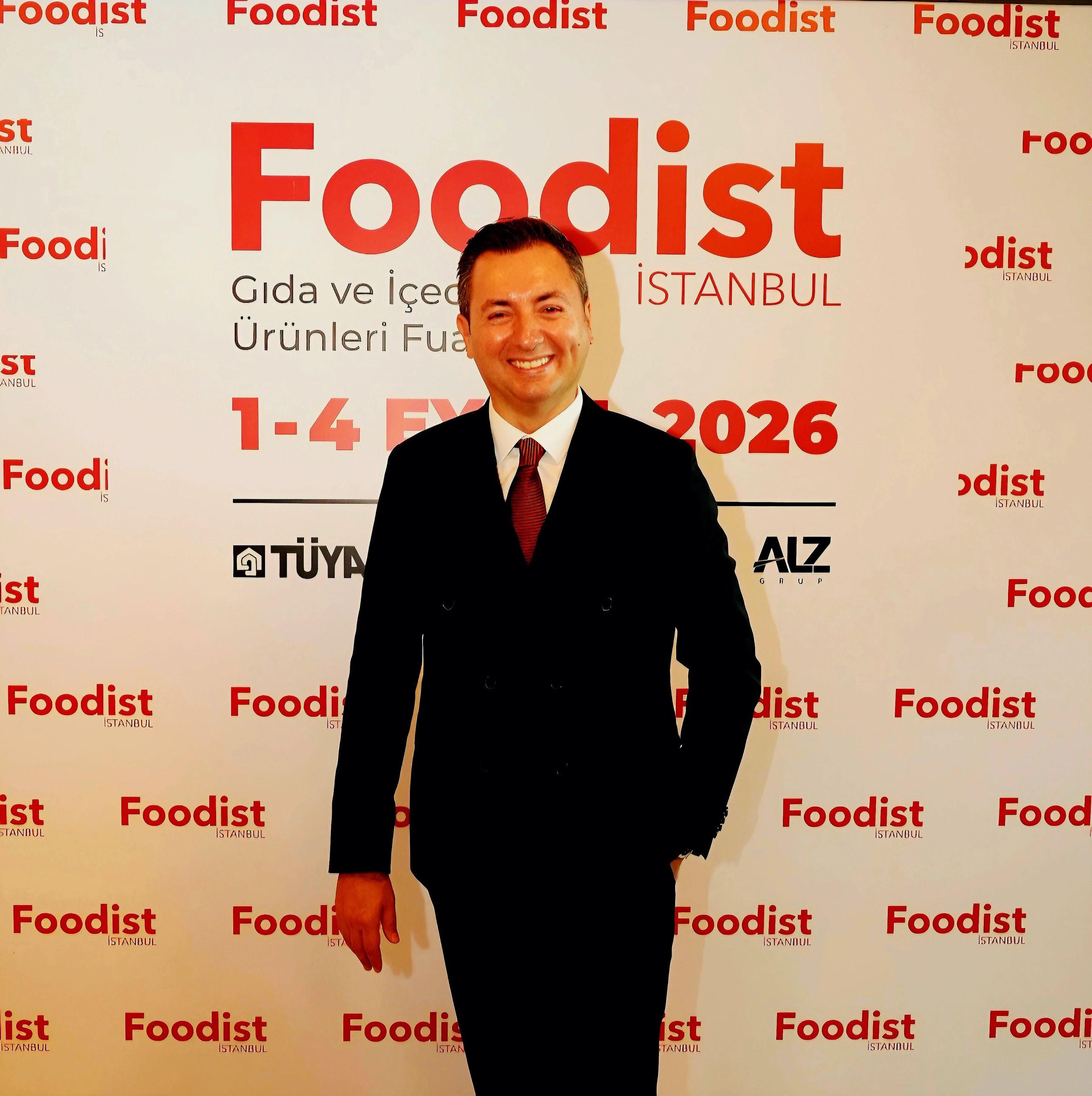 Man in suit smiling at Foodist Istanbul event backdrop.