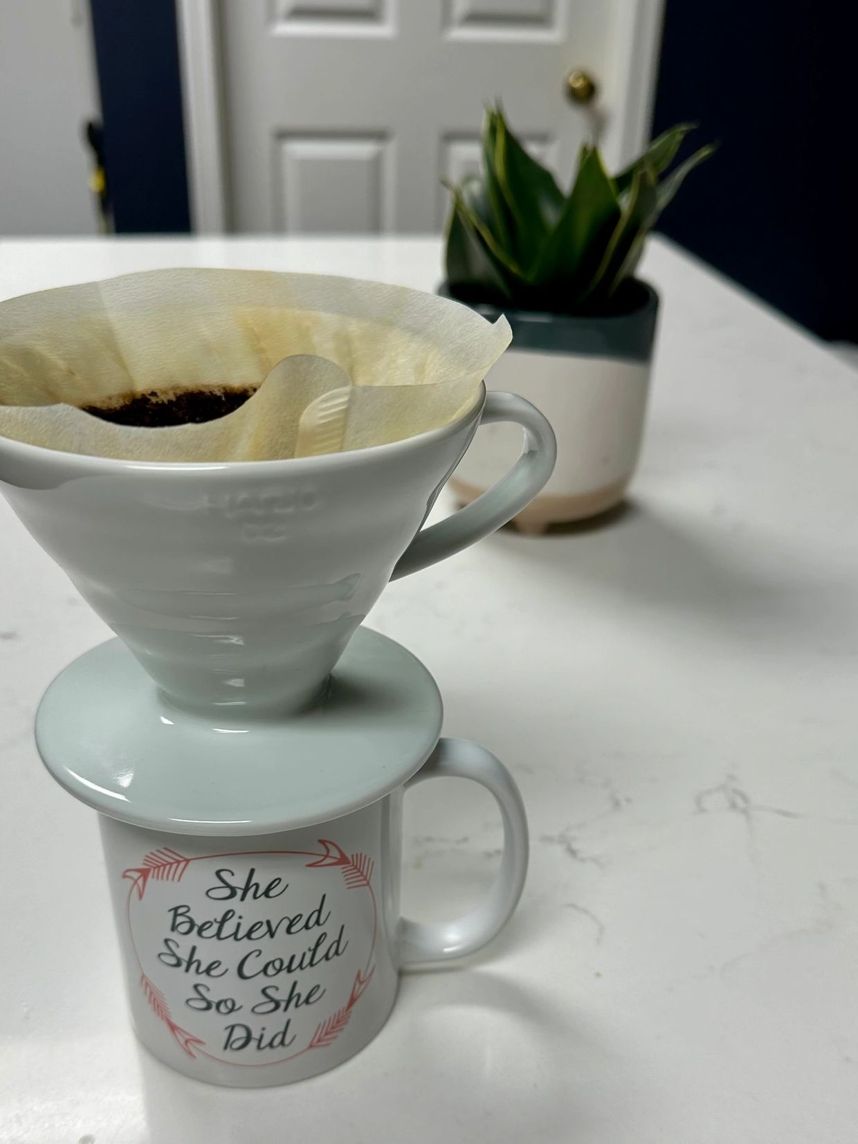 Coffee brewing setup with an inspirational mug on a white countertop.
