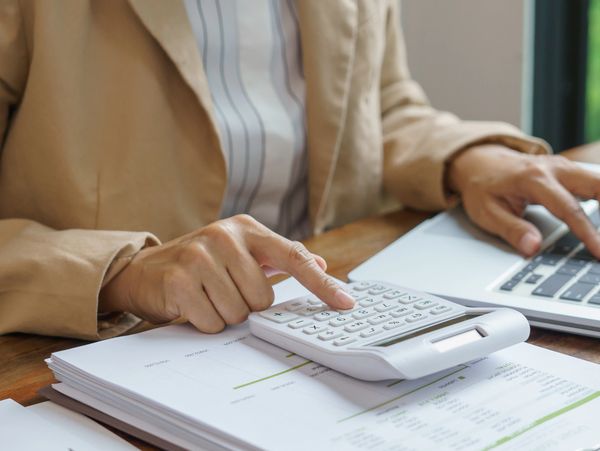 Person using a calculator and laptop at a desk with documents.