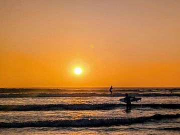 Surfers enjoy the ocean waves during a vibrant sunset.