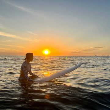 Person with surfboard in water at sunset.