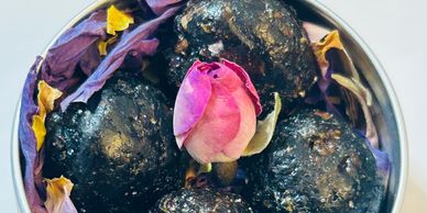 Four handcrafted Kemet Kyphi incense pearls arranged in a tin with dried blue lotus, rose petals,