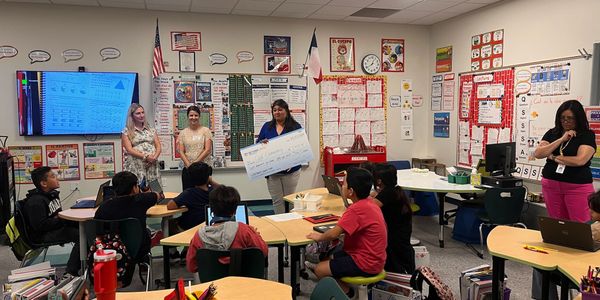 Teacher presenting a large check to a classroom of attentive students.