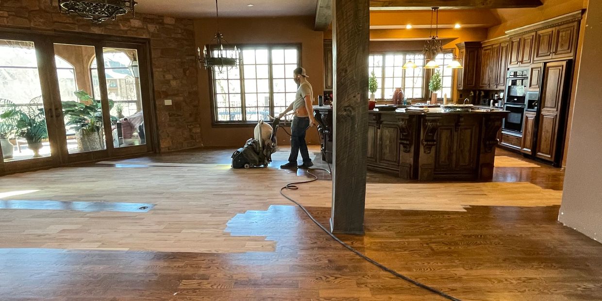 A man sanding the finish and stain off of a hardwood floor.