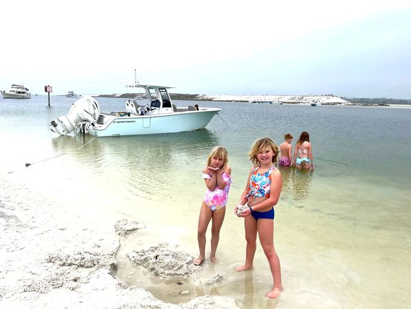 Four children playing by the water near a boat on a cloudy beach day.