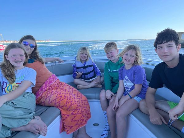 Six kids smiling and relaxing on a boat under clear blue skies.