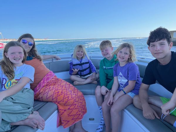 Six kids smiling and relaxing on a boat under clear blue skies.
