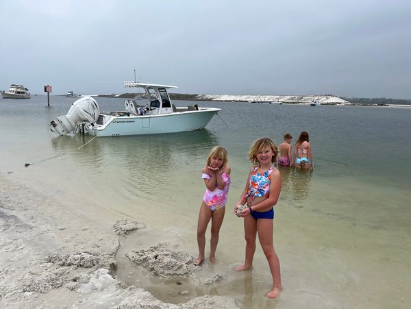 Four children playing by the water near a boat on a cloudy beach day.