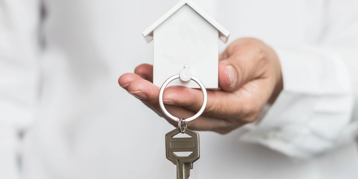 Hand holding a house-shaped key holder with a key attached.