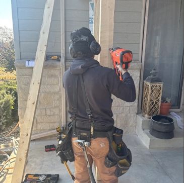 Worker using a nail gun on a house exterior during construction.