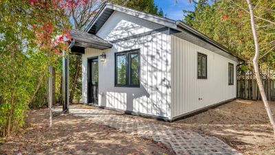 A small modern white house with black window frames surrounded by trees.
