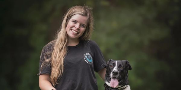 Young woman smiling with her black-and-white dog outdoors.