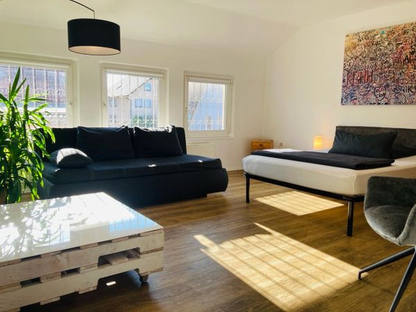Bright, modern studio with black sofa, bed, and natural light.