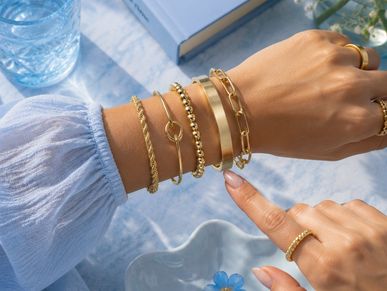 Gold bracelets adorning a wrist with a sheer sleeve.