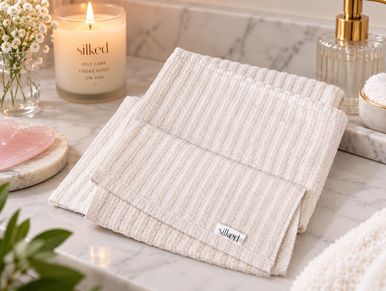 Soft, folded beige towel on a marble surface with candle and decor.