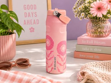 Pink floral Stanley water bottle on a table with decorative items.