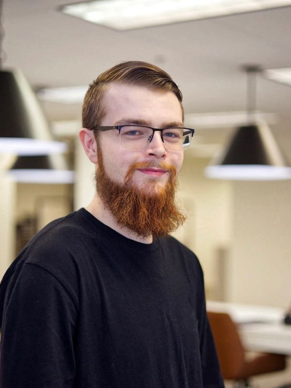 A man with a beard and glasses poses in a professional office setting, showcasing a focused demeanor.