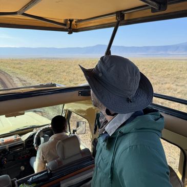 Man in a safari vehicle looking out at the savannah and mountains.