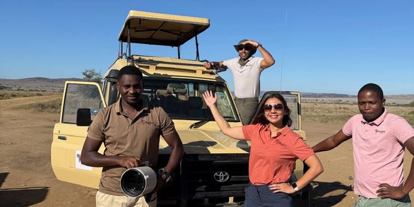 Four people standing by a safari vehicle in a sunny savannah landscape.