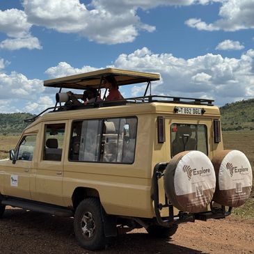Safari vehicle with tourists viewing wildlife under a partly cloudy sky.