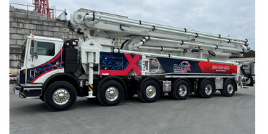 Large white and red concrete pump truck parked on a construction site.