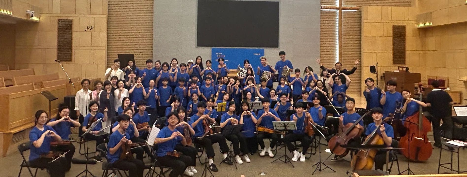 Large group of musicians posing with string instruments and hand signs.