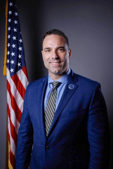 Man in blue suit standing in front of an American flag.