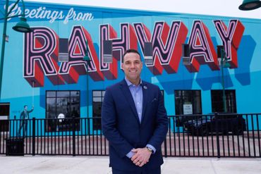 Man in a suit standing in front of a colorful Rahway mural.
