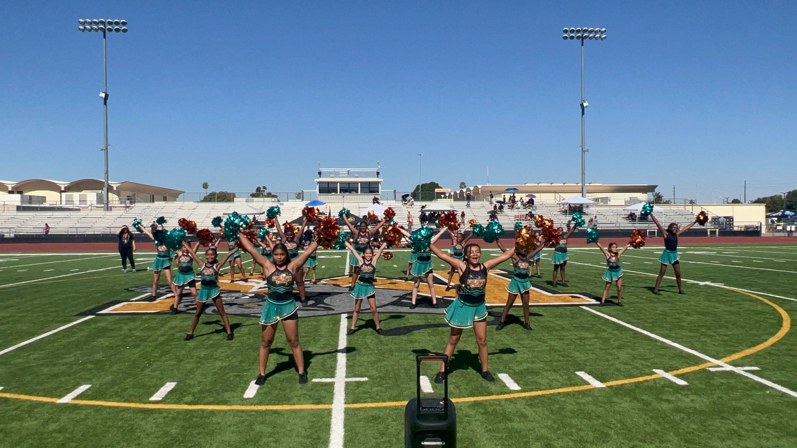 A cheerleading team performs on a football field under clear blue skies.