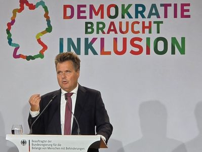Jürgen Dusel am Rednerpult. Im Hintergrund die Umrisse der Bundesrepublik Deutschland und der Text "