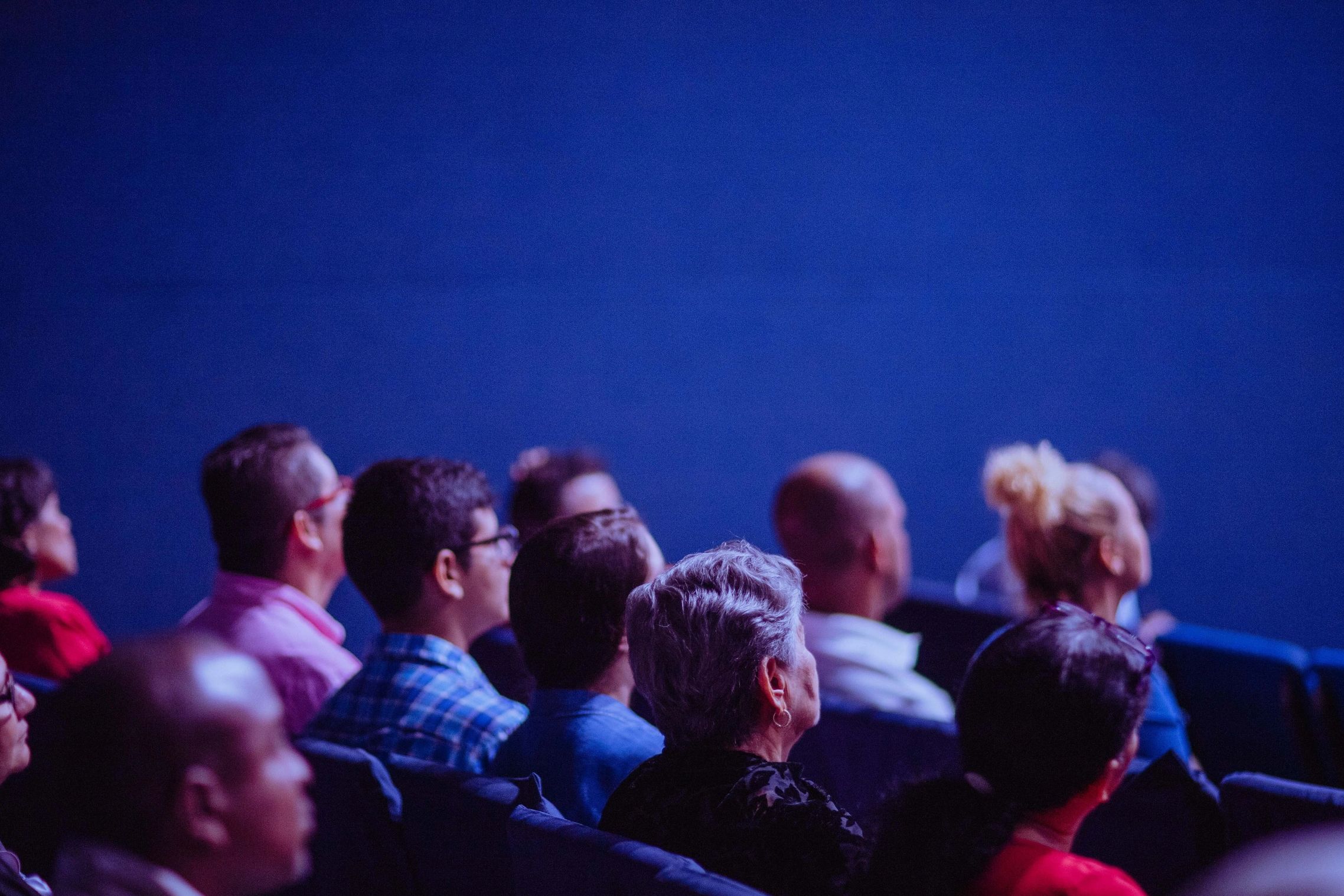 Audience attentively watching a presentation against a blue backdrop.