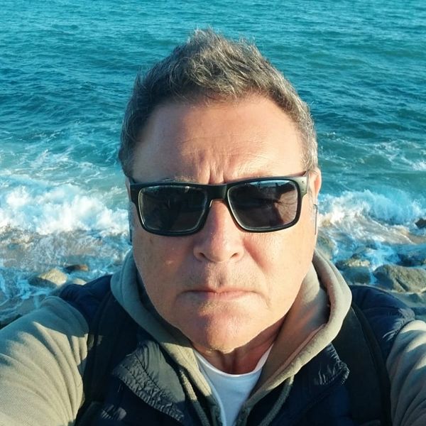 Man wearing sunglasses takes a selfie by the ocean shore.