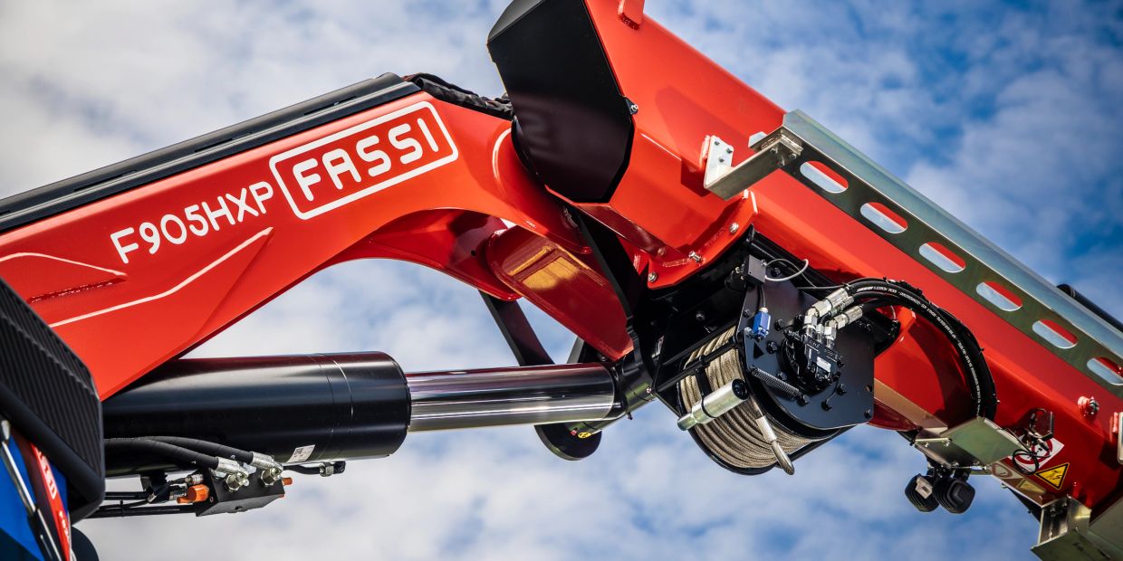 Close-up of a Fassi F905HXP crane arm against a blue sky.