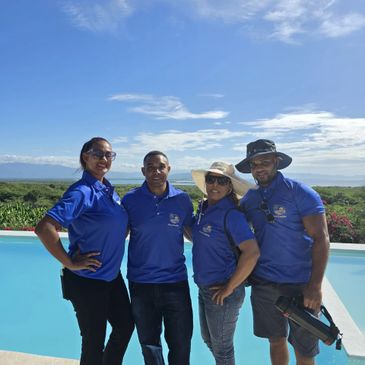 Four people in blue shirts posing by a pool under a sunny sky.
