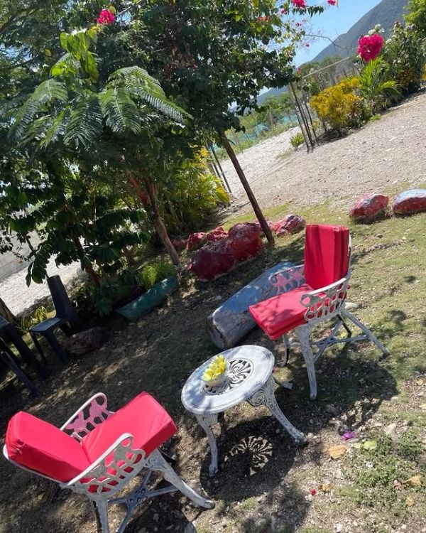 Outdoor garden seating with white chairs and red cushions around a small white table.