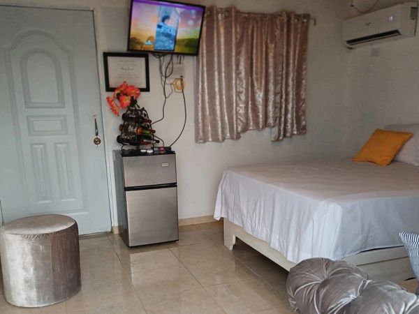 Cozy bedroom with a small fridge, mounted TV, and soft furnishings.