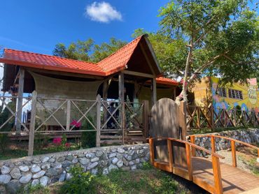 Rustic house with a red roof and wooden bridge under a blue sky.
