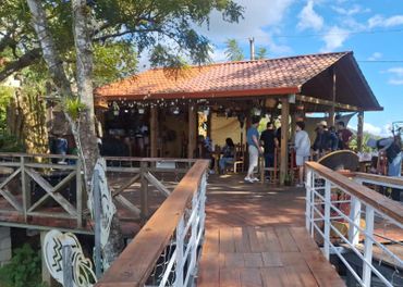 Wooden deck leading to an open-air café under a tiled roof with people gathered.