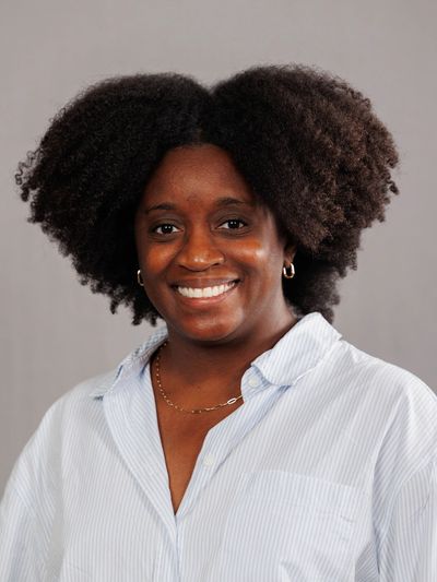 Smiling woman with natural afro hair wearing a white striped shirt.