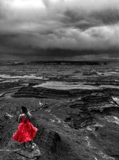 A woman in a red dress stands on dark, rocky terrain under a stormy sky.